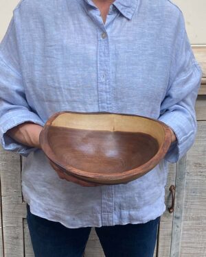 An employee at Spencer Peterman holding a 10-inch Burlwood oval bowl, showing the natural grain and deep figure of the wood.