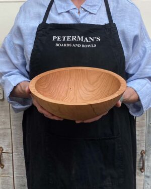 A 10-inch cherry wood round bowl held by a Spencer Peterman craftsperson, the warm tone of the wood glowing in natural light.