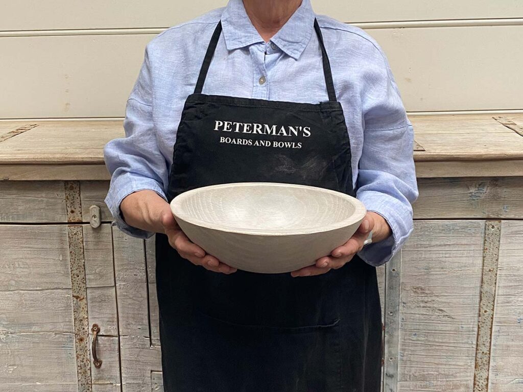 A 10-inch White Pearl Oak round bowl held by a Spencer Peterman craftsperson, with a light pearl finish and subtle natural texture.