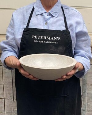 A 10-inch White Pearl Oak round bowl held by a Spencer Peterman craftsperson, with a light pearl finish and subtle natural texture.