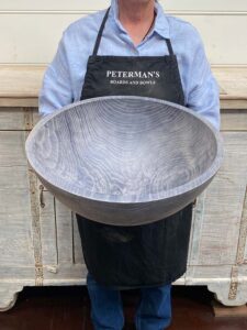 An employee at Spencer Peterman holding an 18-inch Driftwood Oak round bowl, featuring a gently textured surface with pale gray color and visible rings.