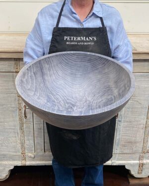An employee at Spencer Peterman holding an 18-inch Driftwood Oak round bowl, featuring a gently textured surface with pale gray color and visible rings.