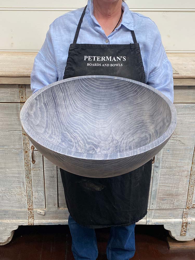 An employee at Spencer Peterman holding an 18-inch Driftwood Oak round bowl, featuring a gently textured surface with pale gray color and visible rings.