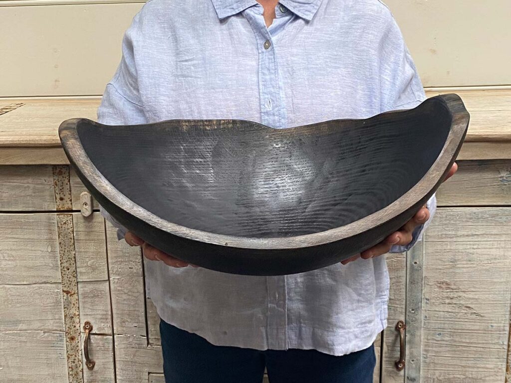 A staff member at Spencer Peterman holding an 18-inch Ebonized Oak oval bowl, finished in a rich black tone that enhances the hand-carved grain pattern.