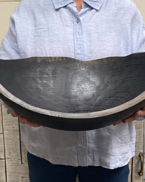 A staff member at Spencer Peterman holding an 18-inch Ebonized Oak oval bowl, finished in a rich black tone that enhances the hand-carved grain pattern.