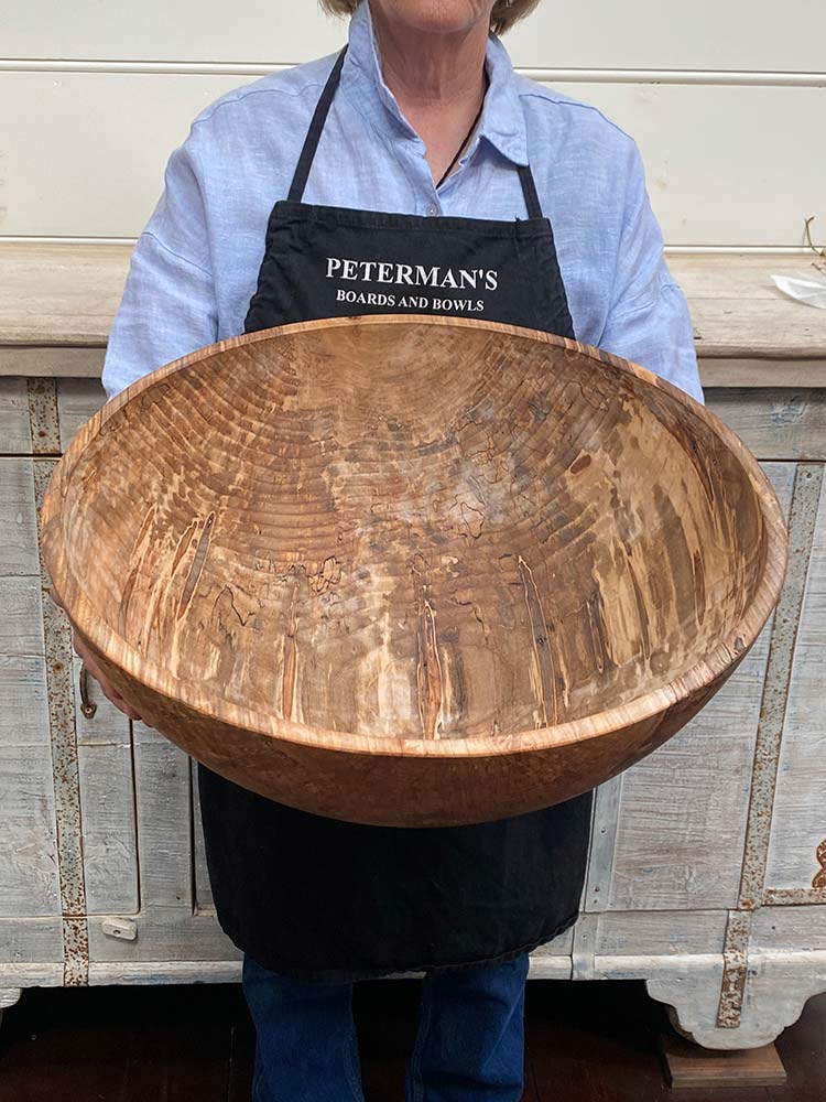 A staff member at Spencer Peterman holding a 21-inch Spalted Ambrosia Maple round bowl, showcasing striking patterns of spalting and ambrosia streaks across the golden maple surface.