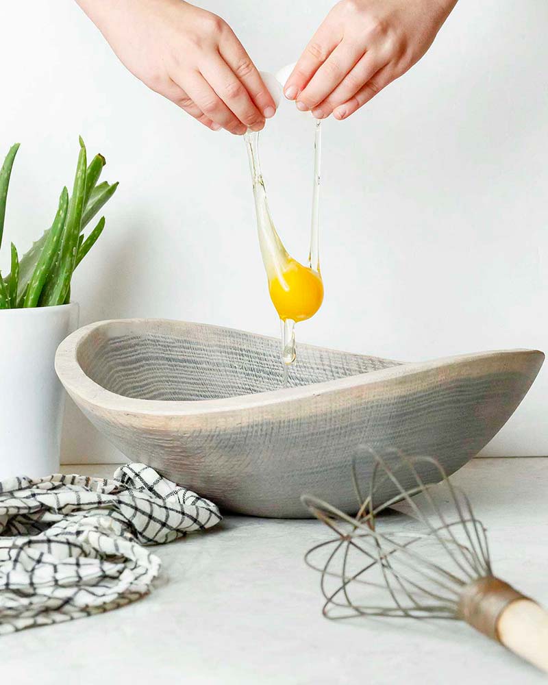 Hands cracking an egg into a food safe driftwood oak wooden bowl, highlighting its use for kitchen prep and natural artisan design