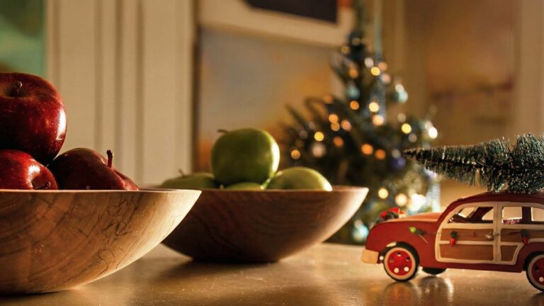 Hand-turned wooden bowls filled with apples on a holiday table, with a small tree and toy car in the background