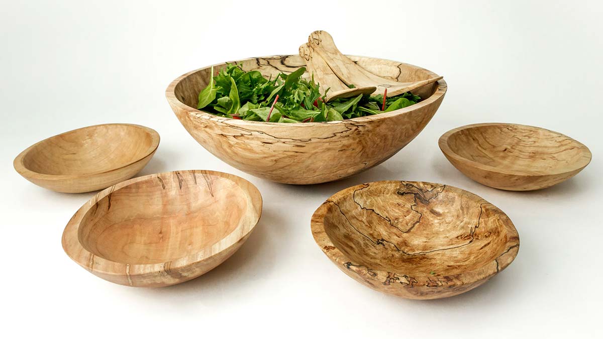 Set of handcrafted wooden salad bowls with a large wooden salad bowl filled with greens in the center.