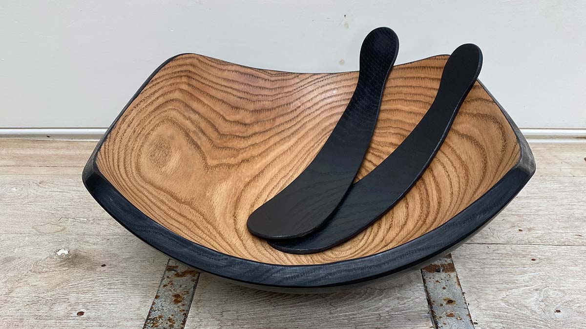 Square wooden serving bowl with two black wooden salad servers resting inside.