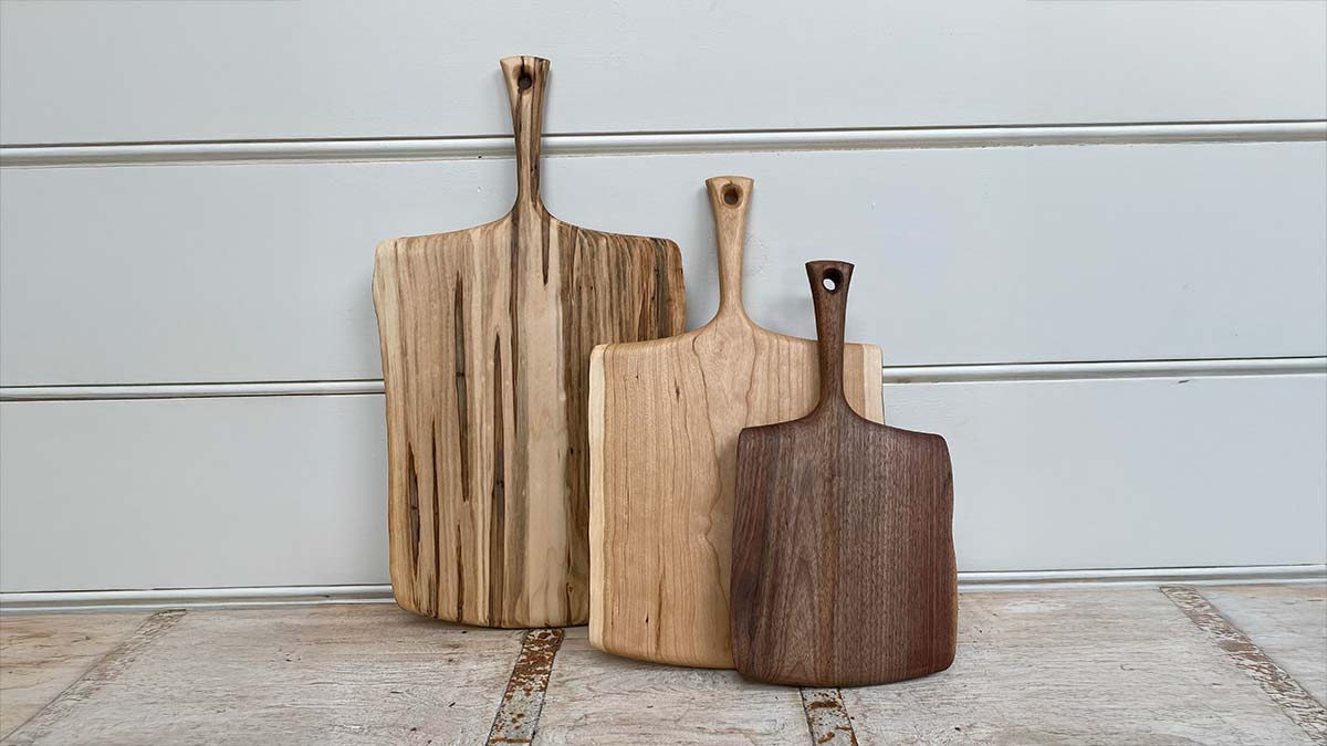Three handcrafted wooden serving boards in different woods leaning against a wall