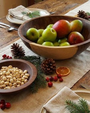 Wooden serving bowls filled with apples and nuts arranged along a holiday table runner
