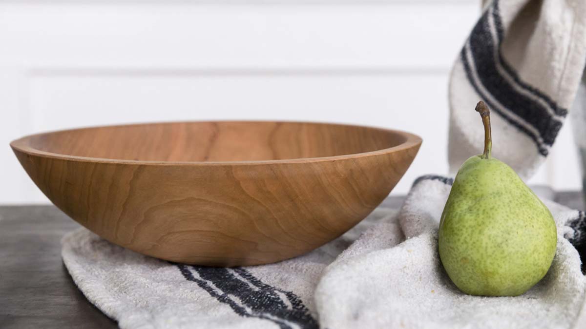 Hand-turned wooden bowl resting on a linen towel beside a green pear in soft winter light
