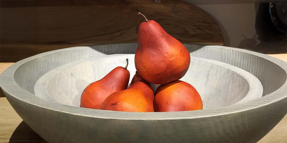 Hand-turned wooden bowl filled with pears resting on a work surface in warm studio light