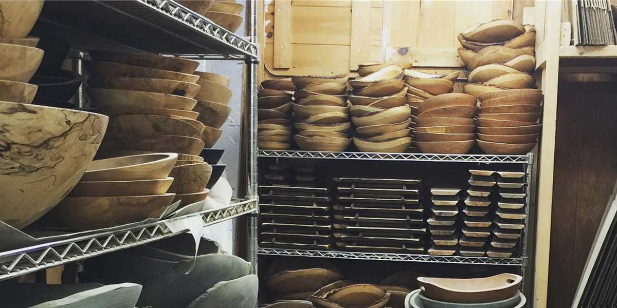 Shelves of unfinished wooden bowls and boards stacked in the workshop
