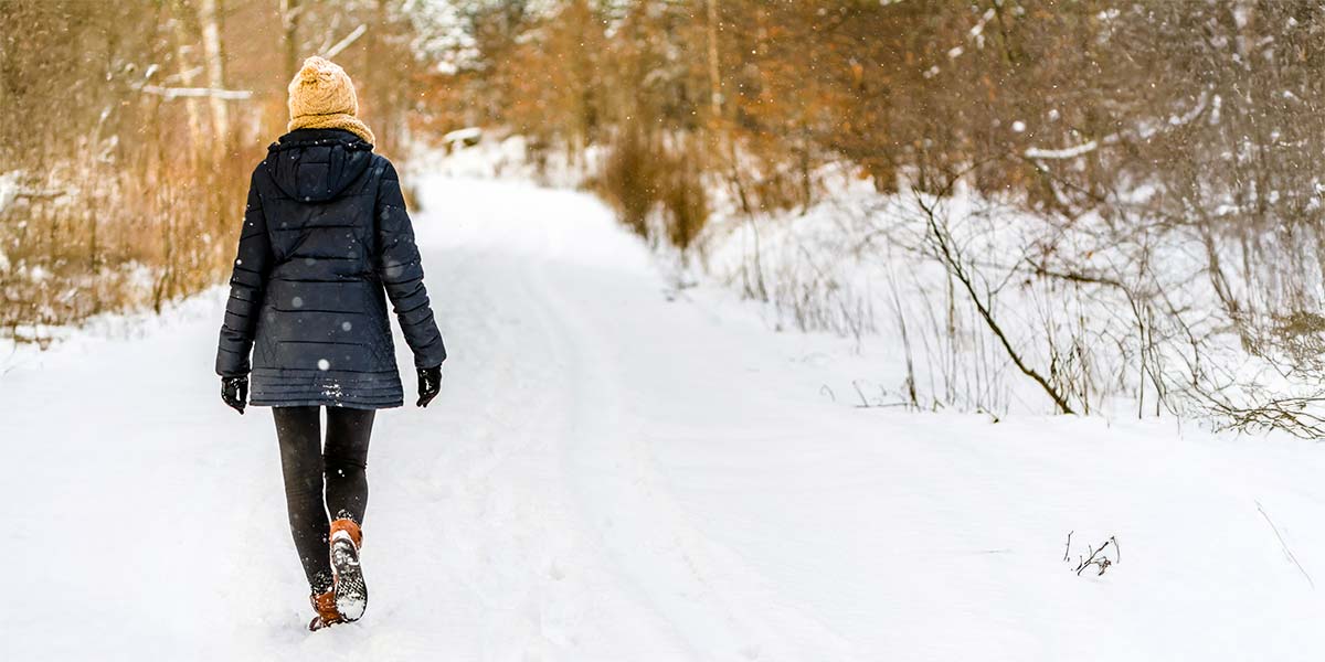 Person walking along a snowy path through winter woods in New England