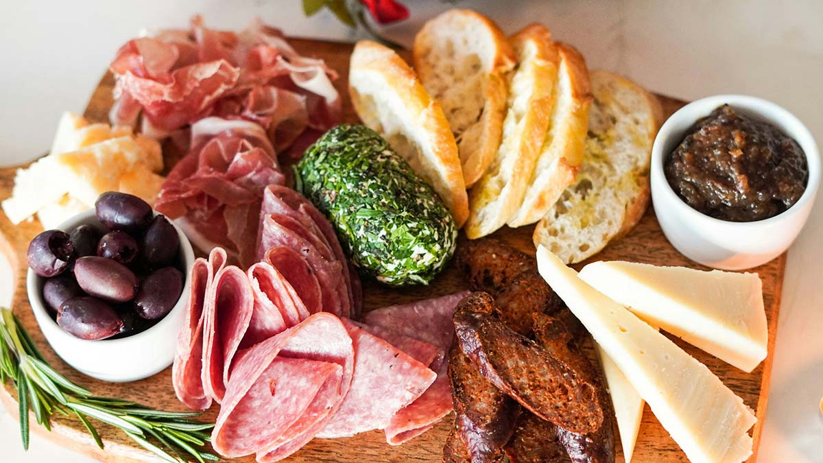 Charcuterie board ideas with salami, olives, cheese, and sliced baguette arranged on wood