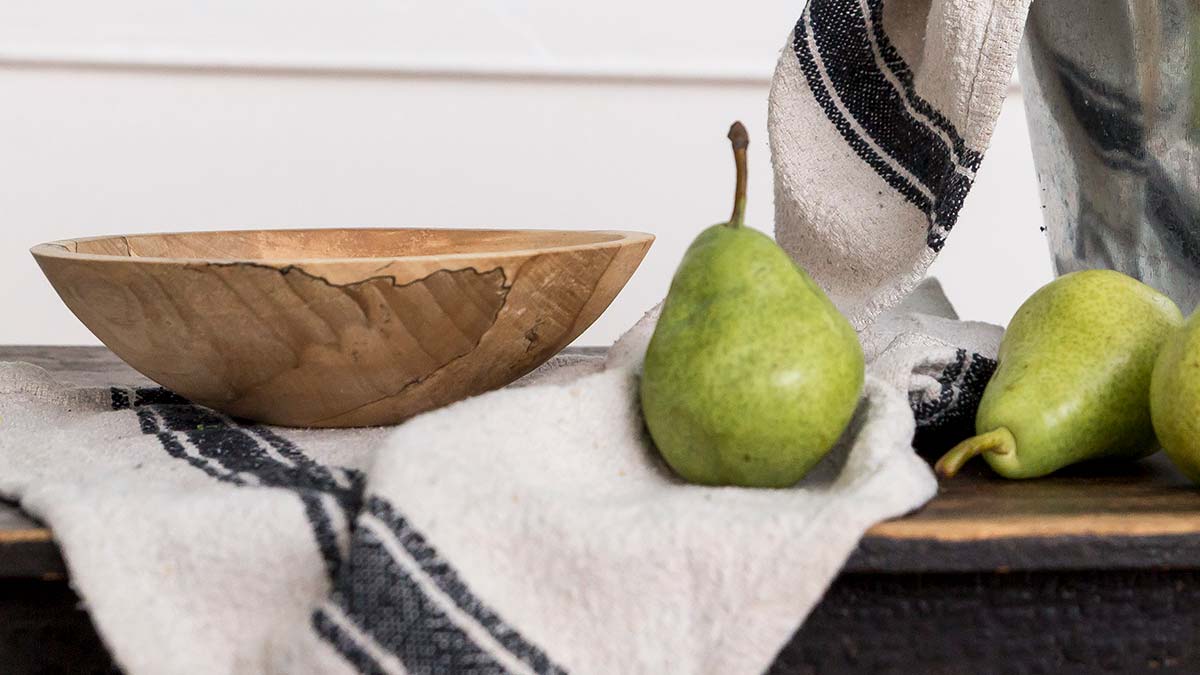Small handcrafted wooden bowl beside fresh pears on a kitchen counter