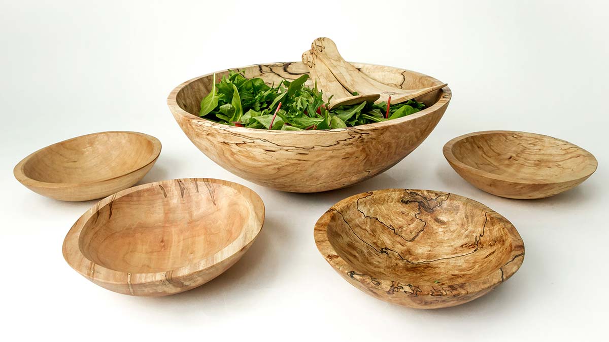 Large spalted maple wooden salad bowl filled with greens and surrounded by matching smaller bowls