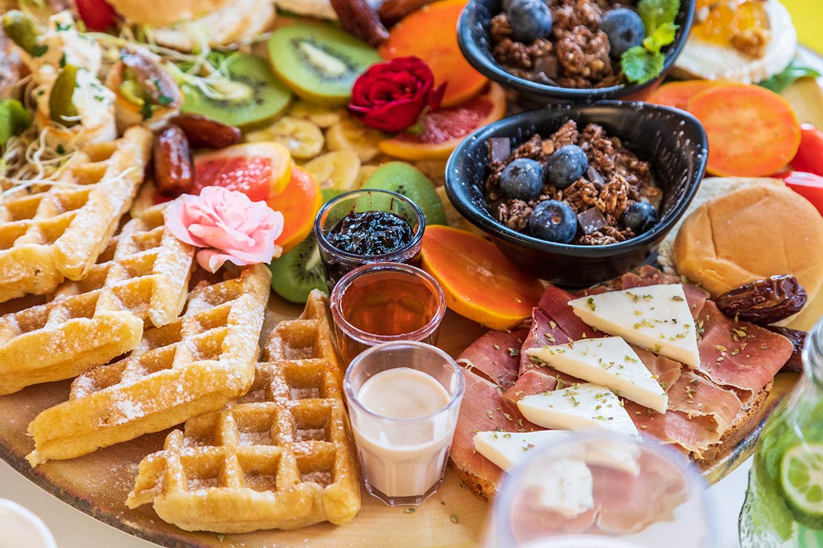 breakfast charcuterie board with waffles, berries, granola, yogurt, and cured meats on a wooden board