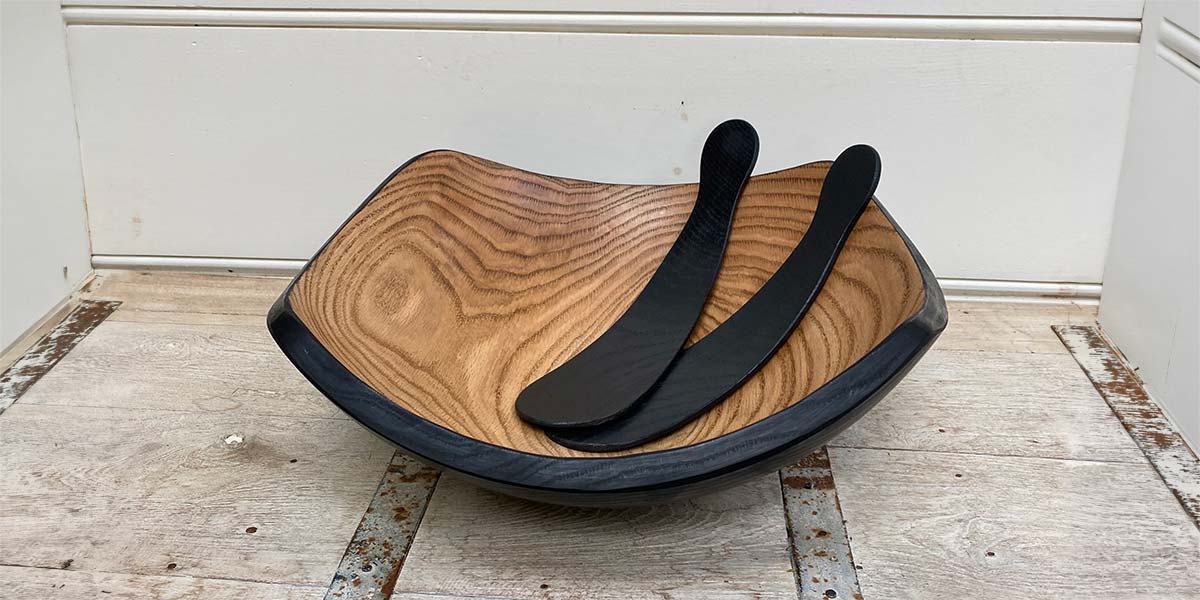 Square wooden serving bowl with contrasting dark rim and matching wooden salad servers